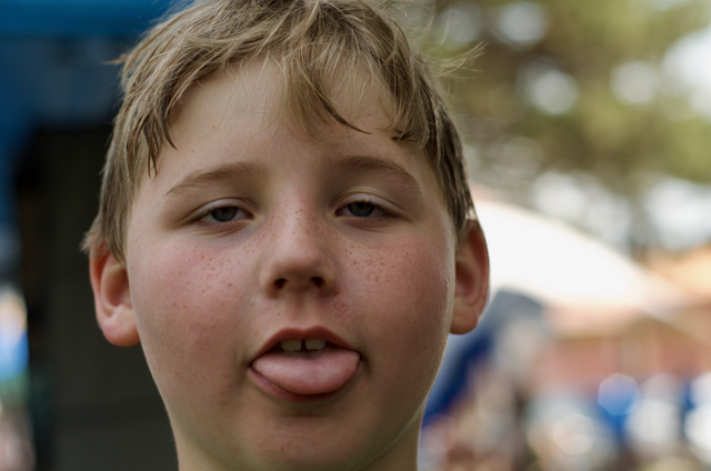 Boy with blond hair sticking out his tongue, looking directly at the camera.