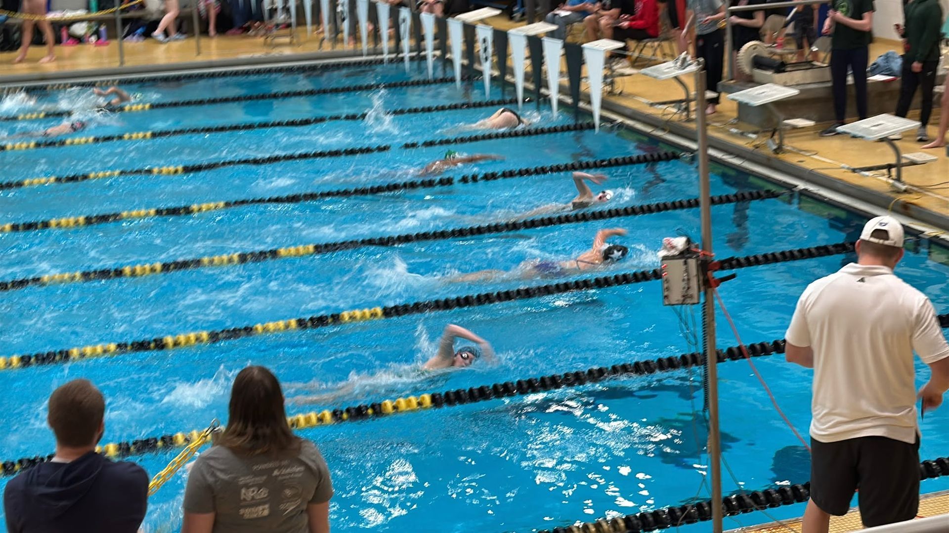 Swimmers racing in a pool during a competition, viewed from an angle.
