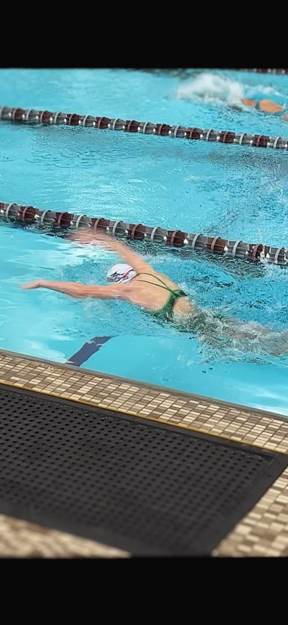 A swimmer in a green swimsuit swims in a pool, doing the freestyle stroke.