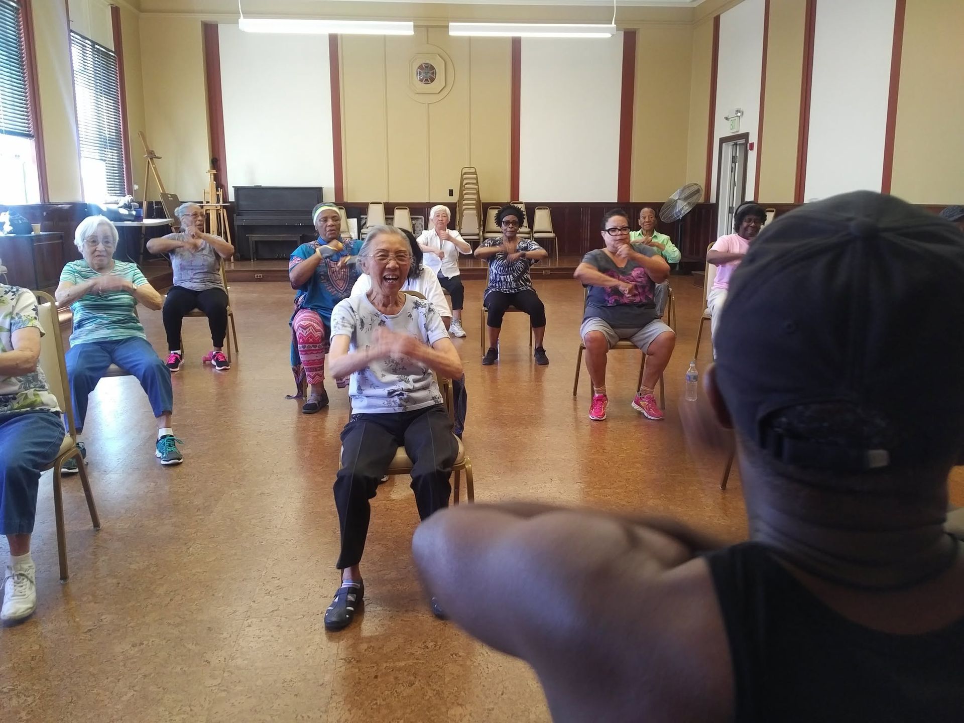 People seated in a hall doing an exercise class, following an instructor in the foreground.