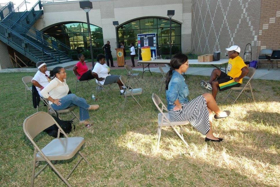 People seated in folding chairs outdoors on a grassy area near a building entrance