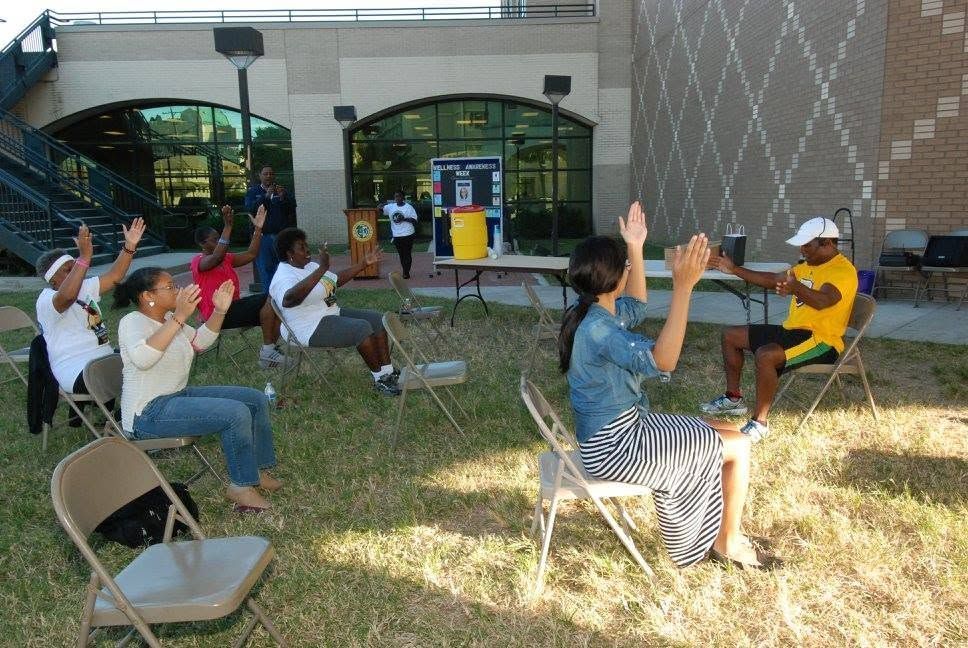 People seated outdoors under a canopy, raising hands during a group activity.