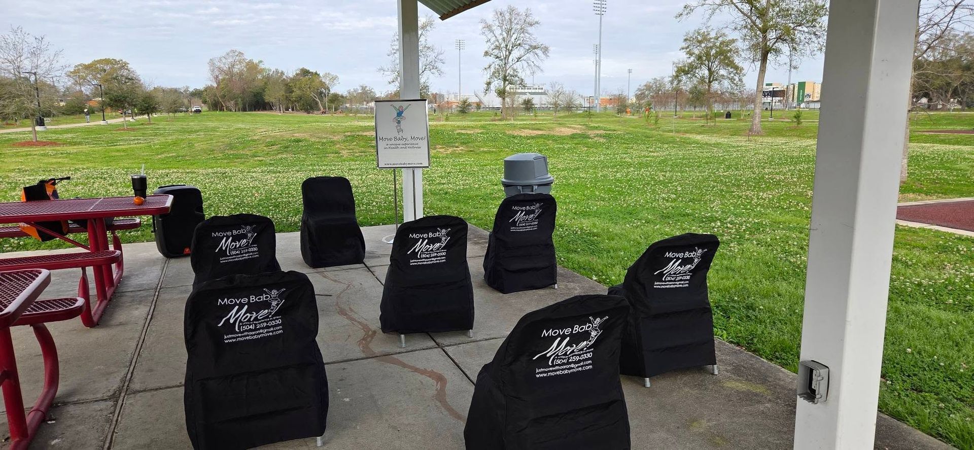 Black beanbag chairs under a pavilion beside a red picnic table, overlooking a grassy park