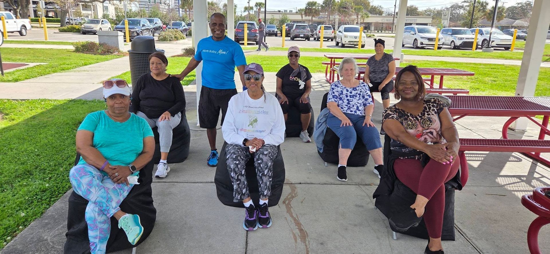 Group of people sitting on benches under a park shelter, posing for a photo on a sunny day.