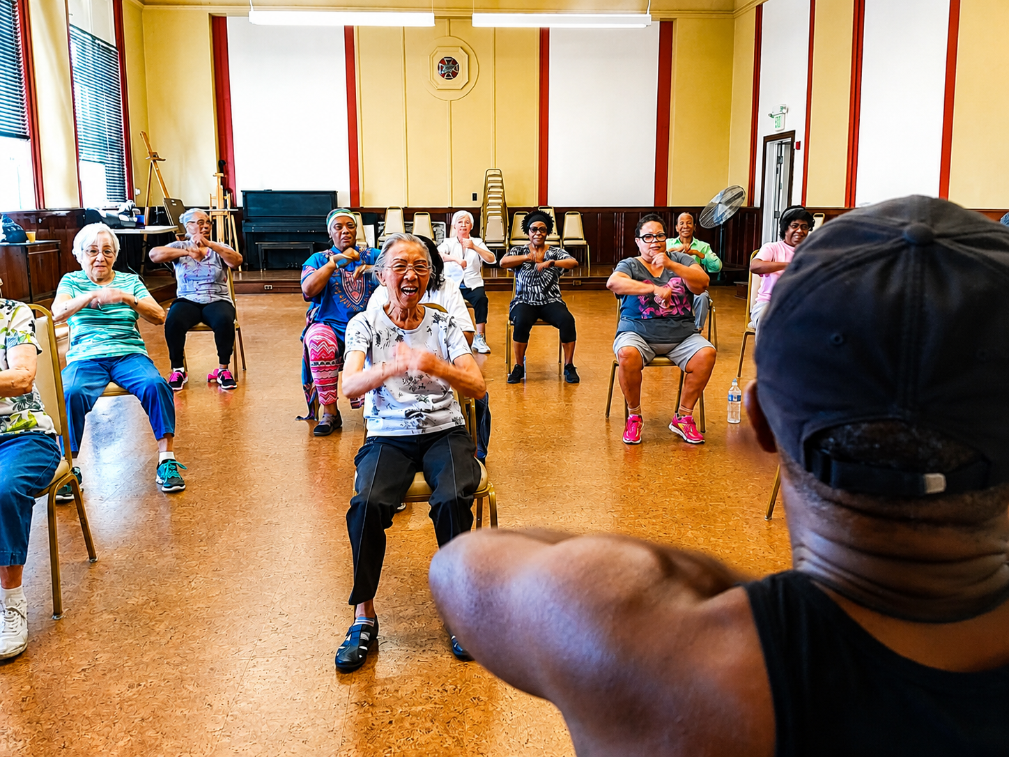 Group exercise class in a bright room, with an instructor leading seated participants.
