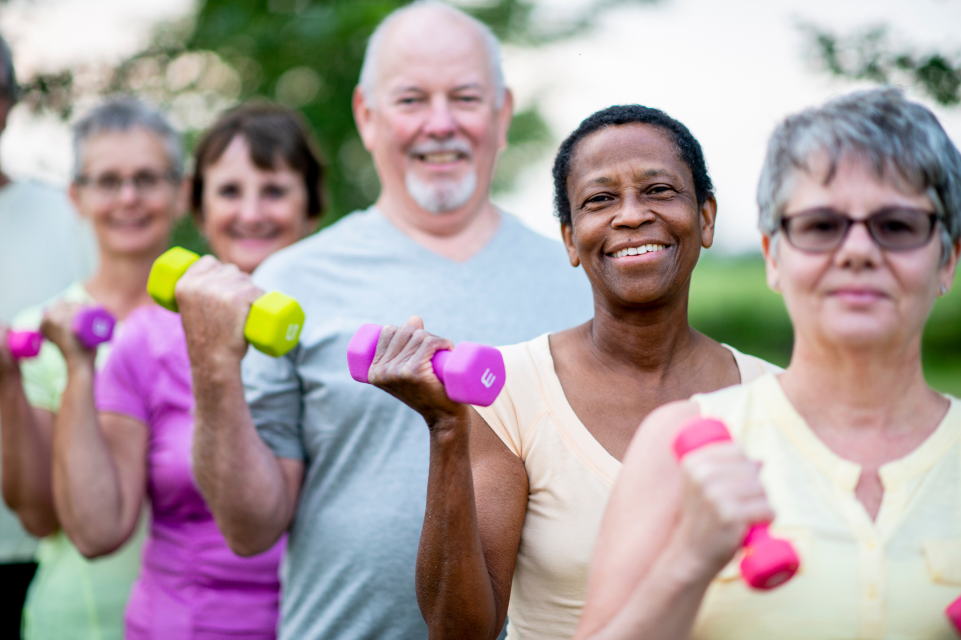 Group doing outdoor dumbbell exercises with smiling faces and colorful weights
