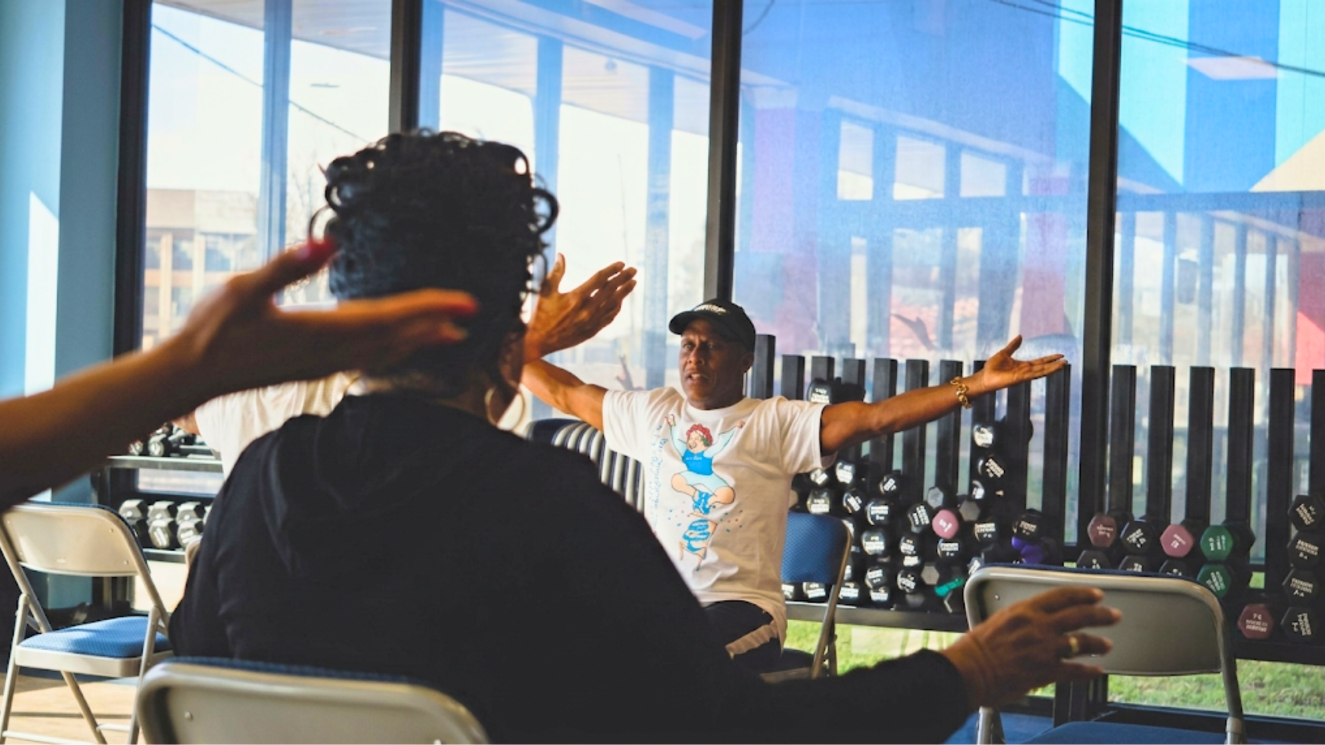 Person using green dumbbells during a physical therapy exercise with a trainer in the background