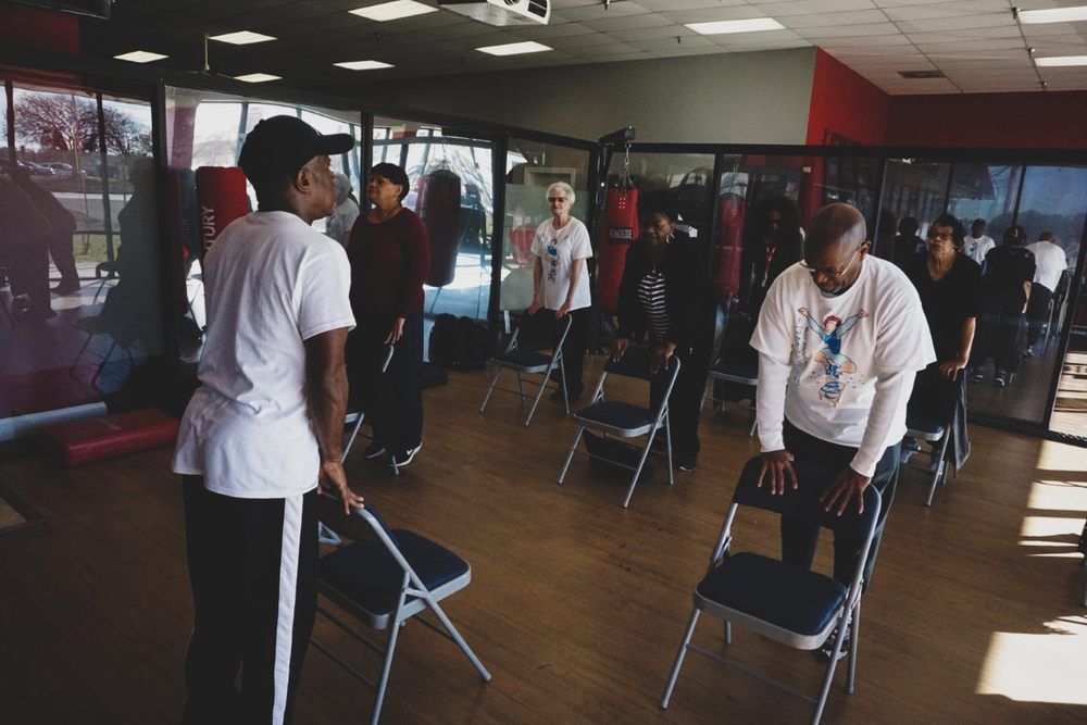 People stretching in a fitness studio with mirrored walls and folding chairs.