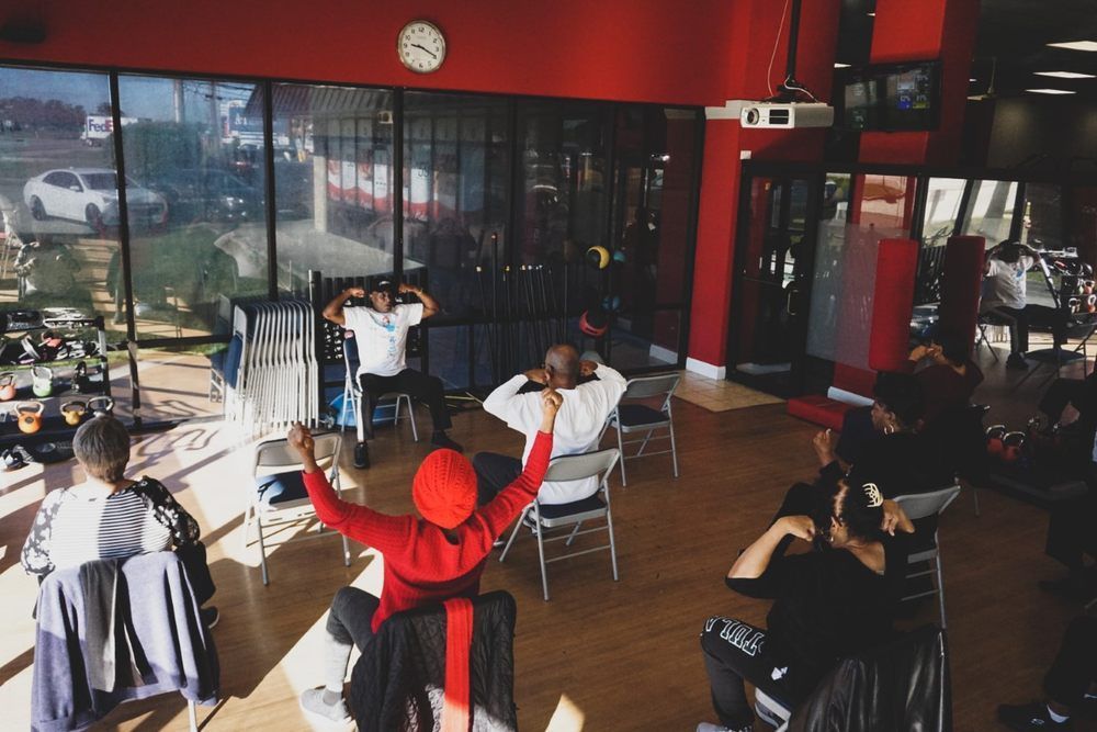 People exercising in a bright gym with mirrors, weights, and red walls