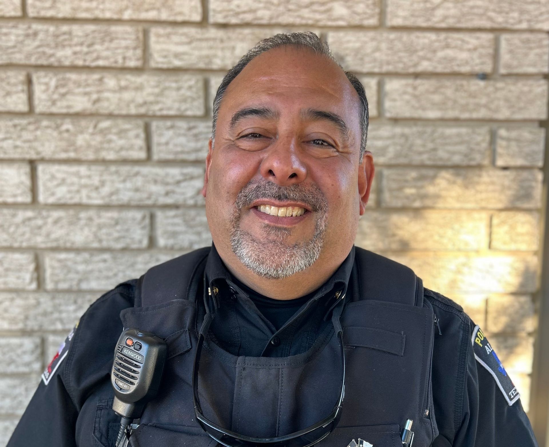 A man in a police uniform is smiling in front of a brick wall.