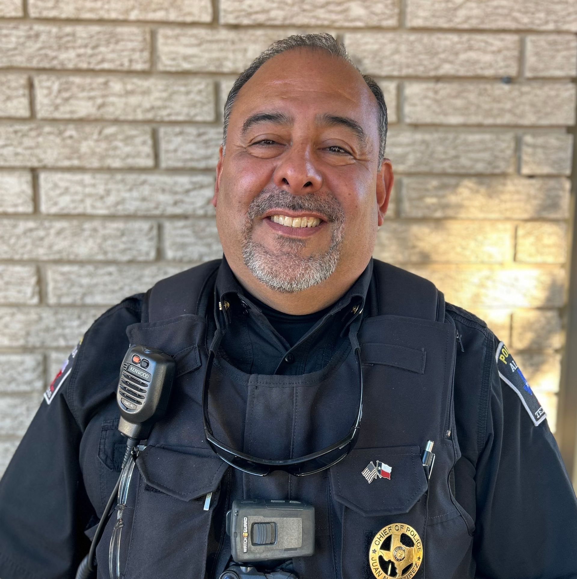 A man in a police uniform is smiling in front of a brick wall.