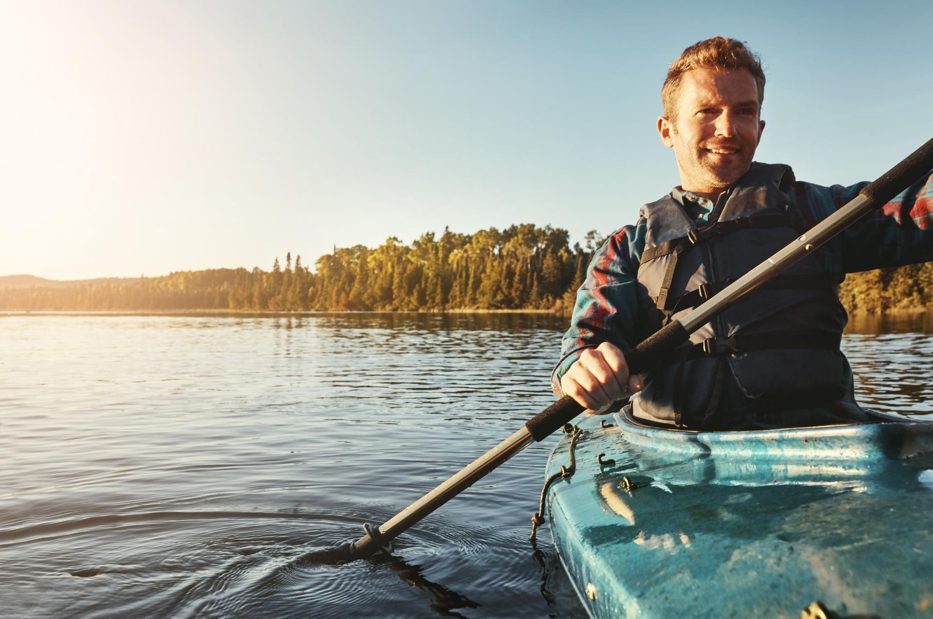 Person kayaking on calm water at sunset, with trees along the shoreline.