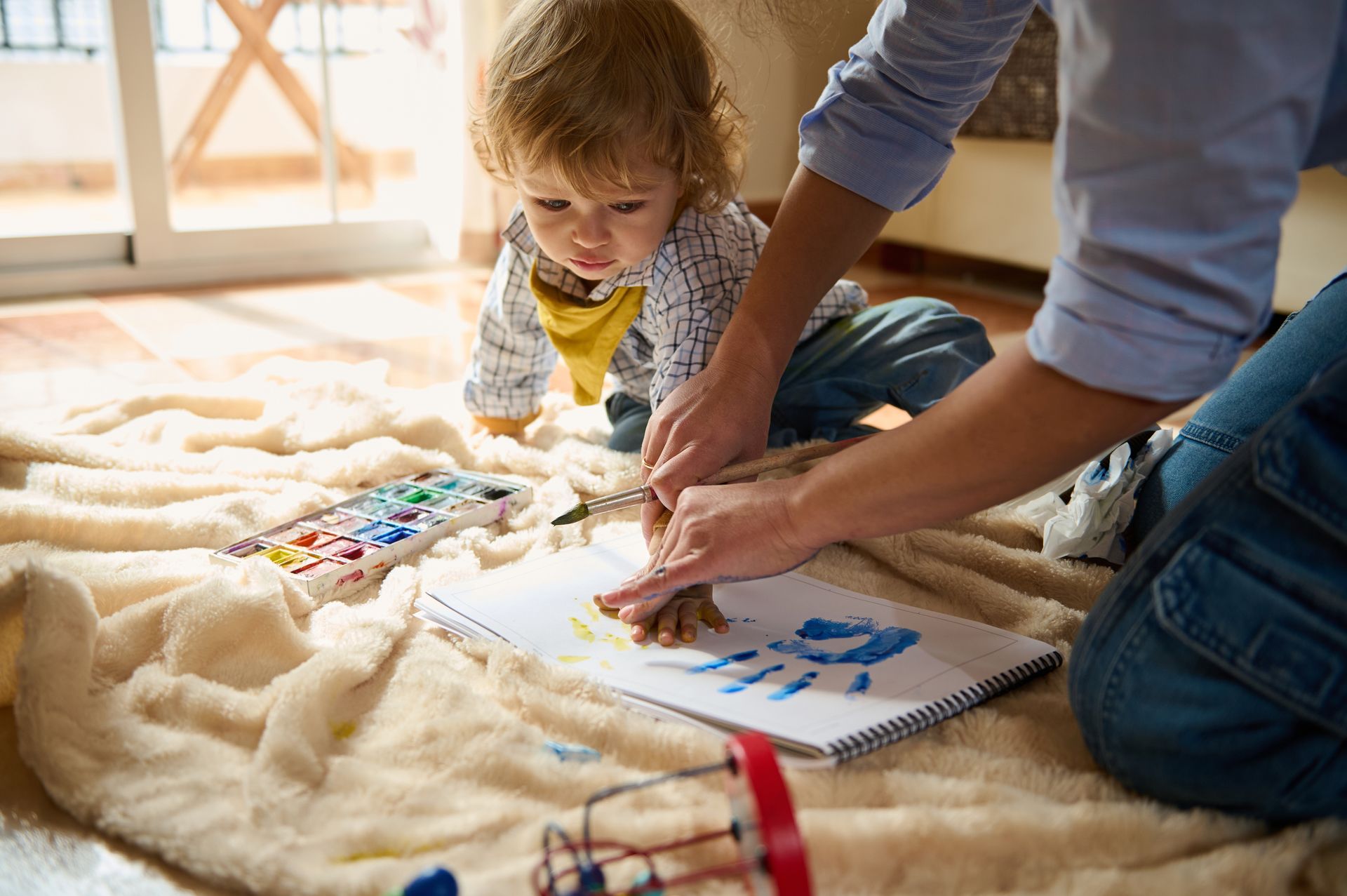 Adult and toddler painting on paper at a cozy indoor play area
