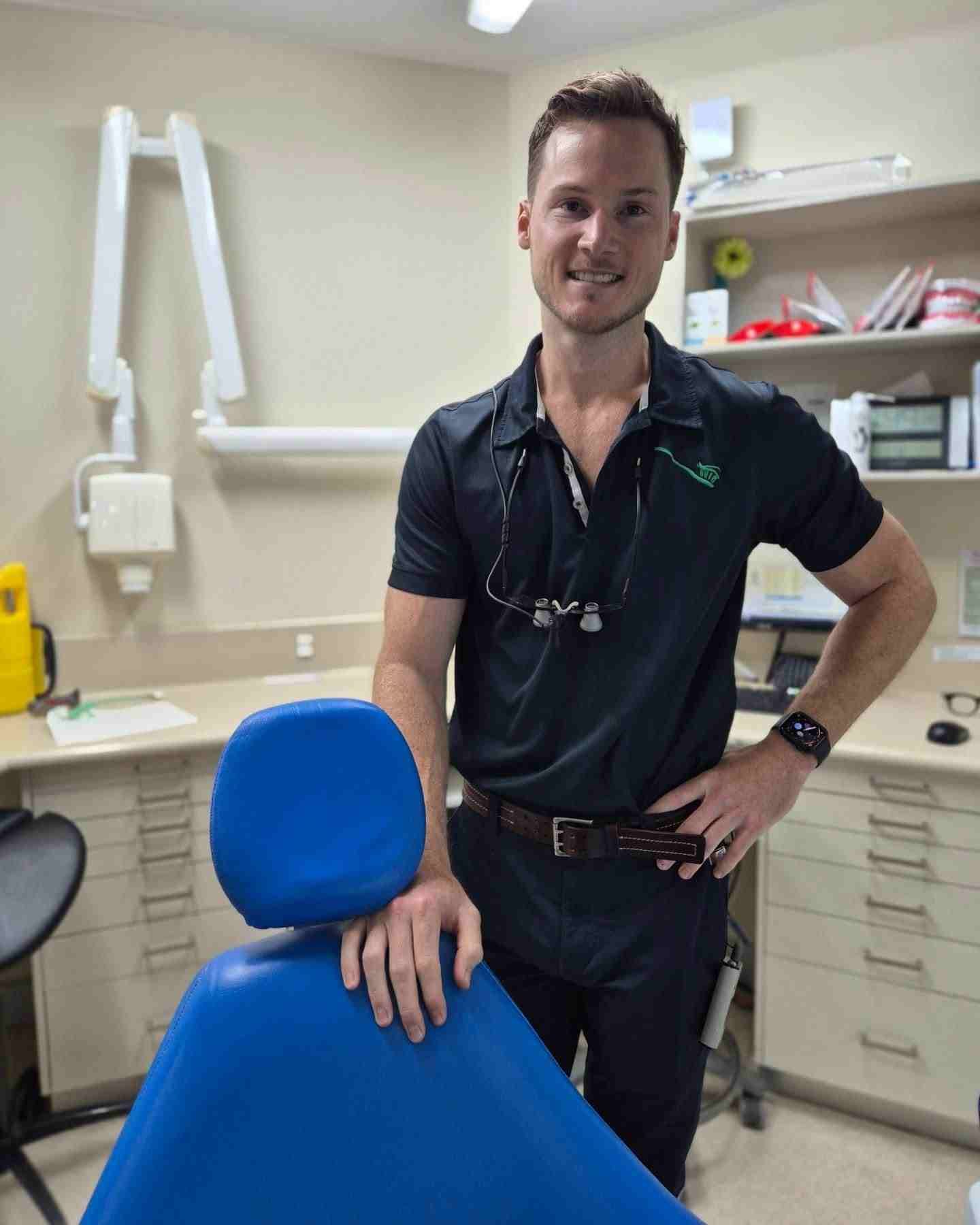 A Man in a Black Shirt is Standing Next to a Blue Dental Chair — Cairns Precision Dental Group In Woree, QLD