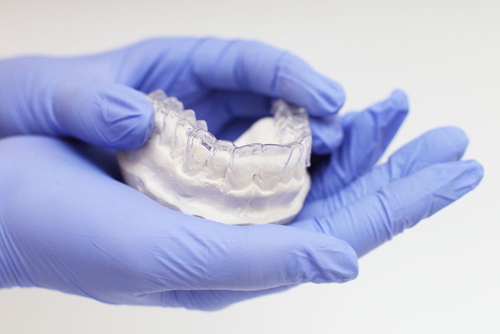 A Person Wearing Blue Gloves Is Holding A Model Of Teeth — Cairns Precision Dental Group In Woree, QLD