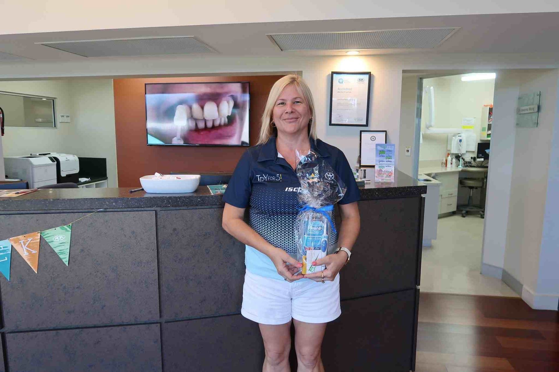 A Woman is Standing in Front of a Counter in a Dental Office Holding a Gift Bag — Cairns Precision Dental Group In Woree, QLD