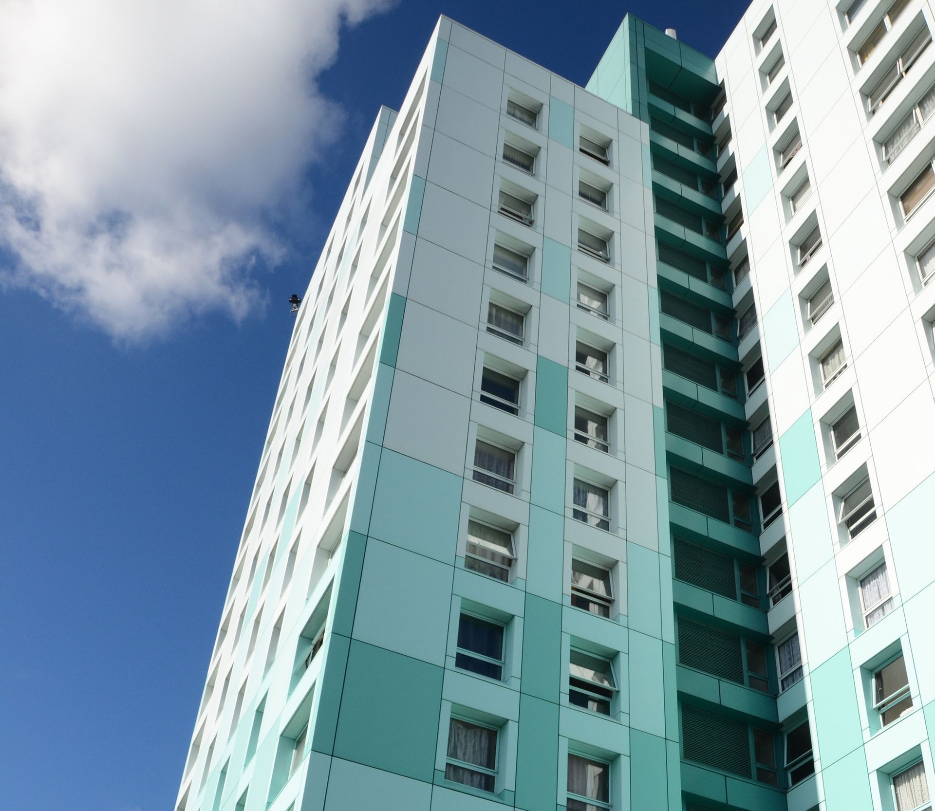 Tall turquoise and white apartment building against a blue sky with clouds.