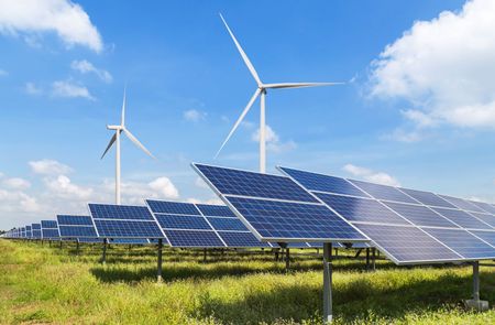 Solar panels and wind turbines in a grassy field under a blue sky.