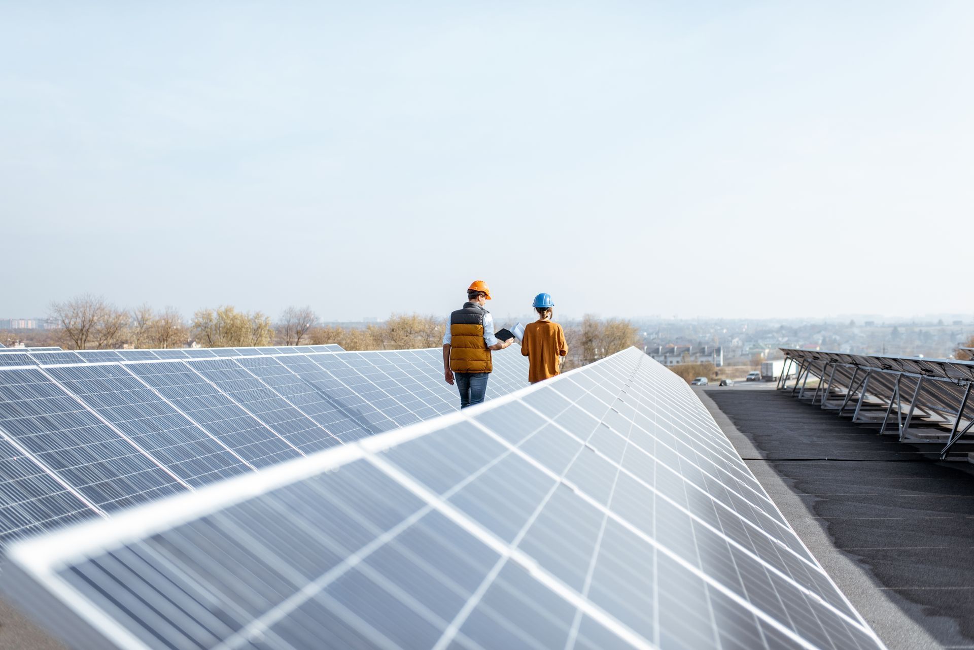 Two people with hard hats walking on rooftop solar panels, inspecting them.