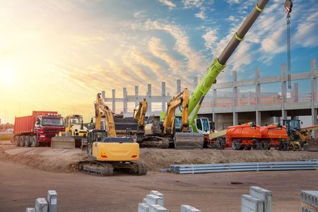 Construction site with excavators, a crane, and concrete structure under construction at sunset.