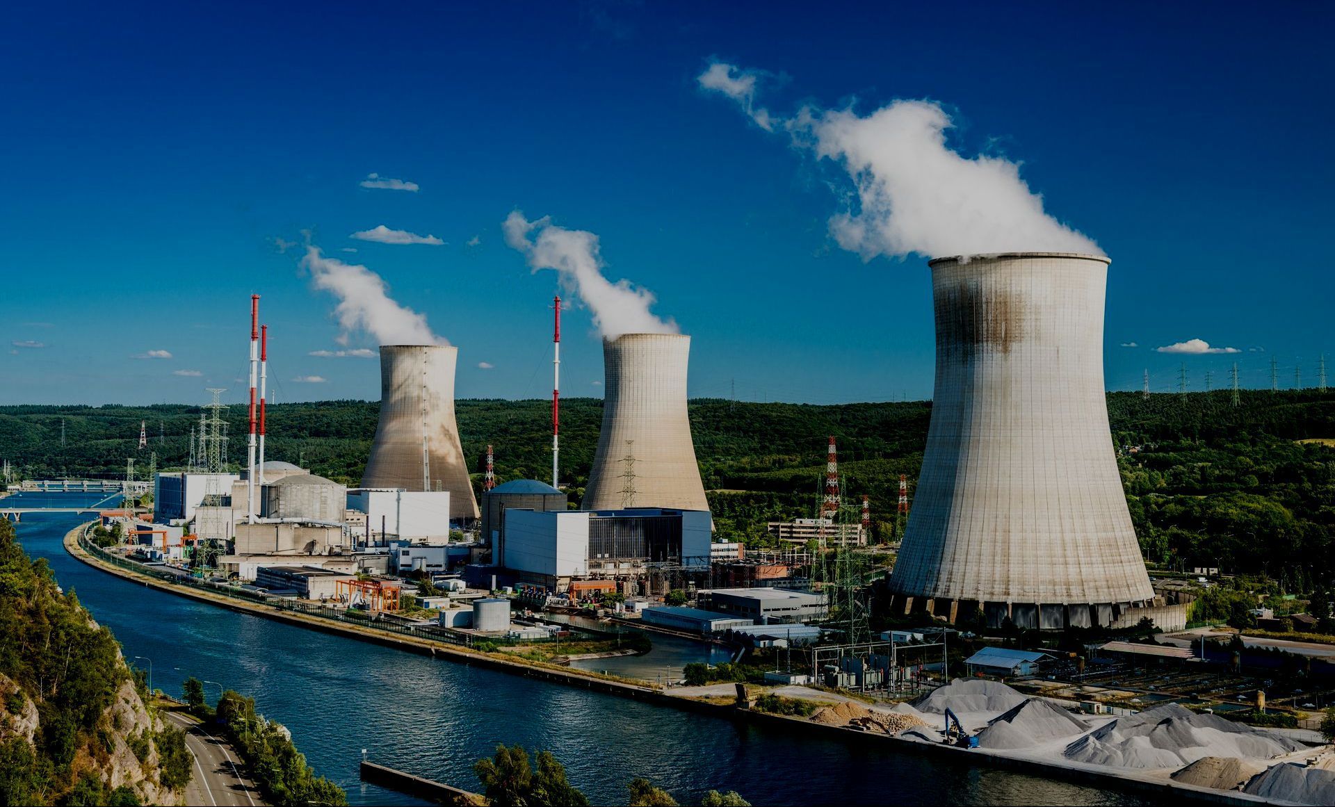 Nuclear power plant with three cooling towers emitting steam, blue sky.