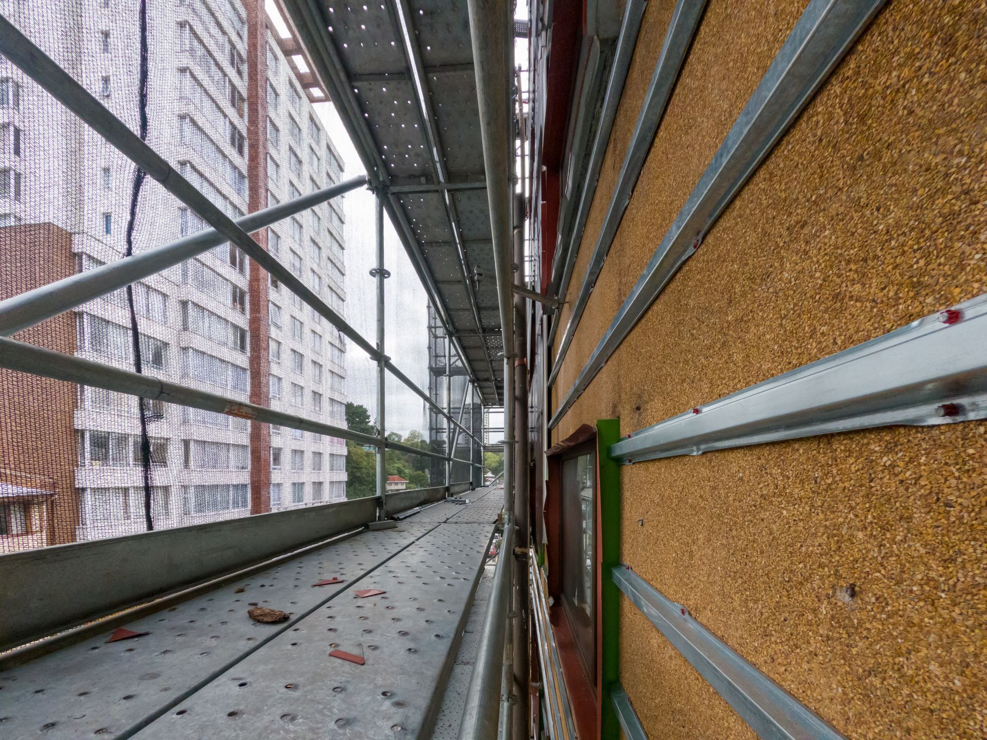 Scaffolding along a building facade, with protective netting and insulation panels visible.