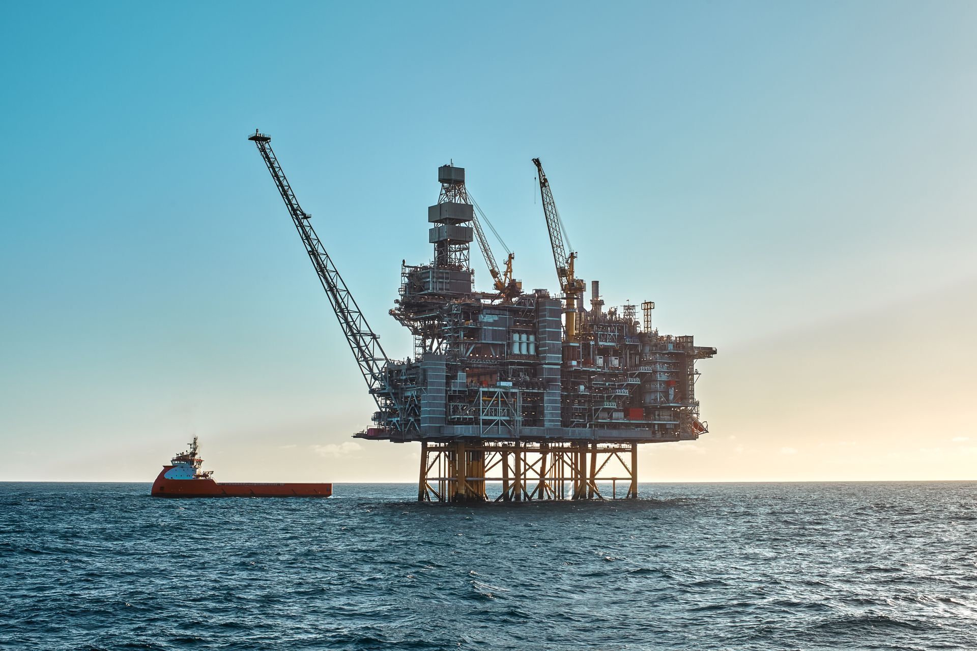 Offshore oil rig in the sea with a supply ship under a blue sky.