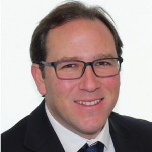 Man in glasses and suit smiling, likely a professional headshot.