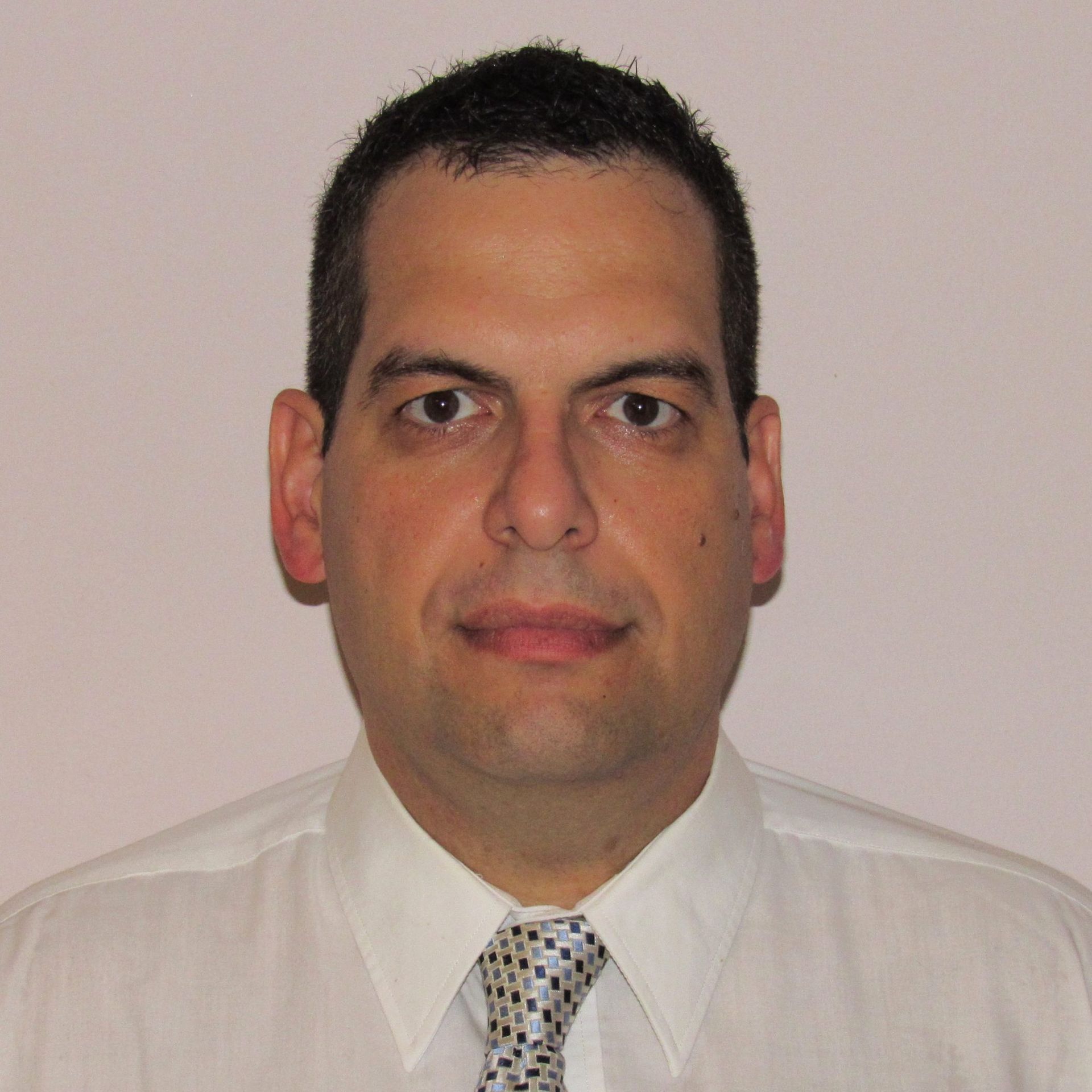 Man in white shirt and tie, looking directly at the viewer, against a plain background.