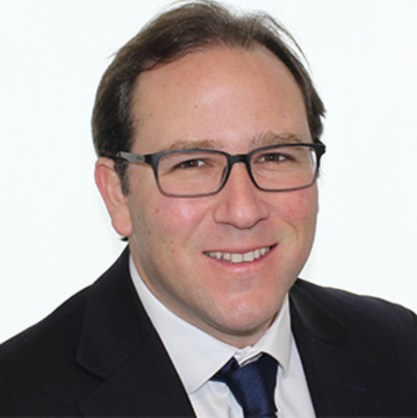 Man with glasses wearing a dark suit and tie, smiling.