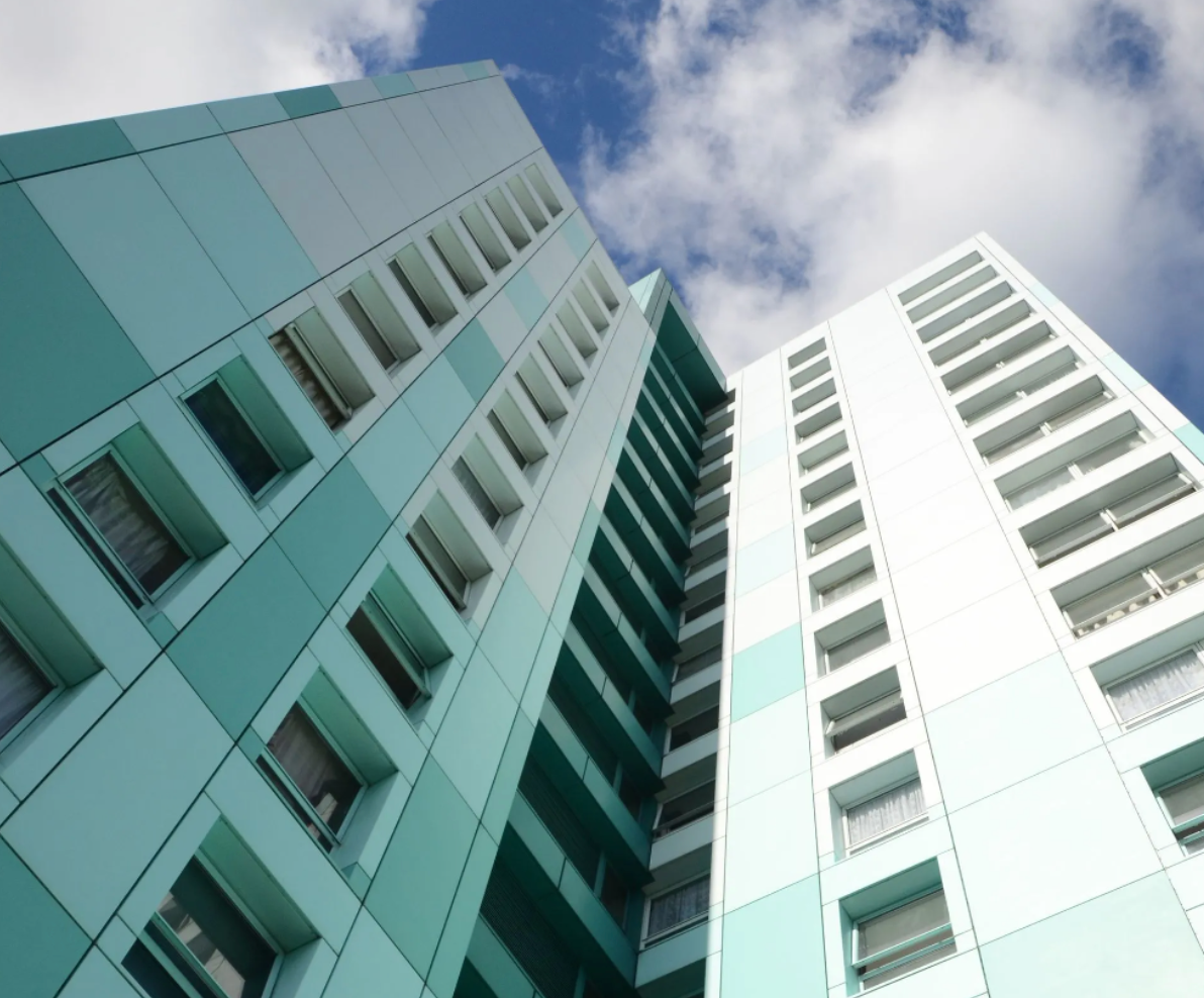 Two tall, turquoise and white apartment buildings against a cloudy blue sky.