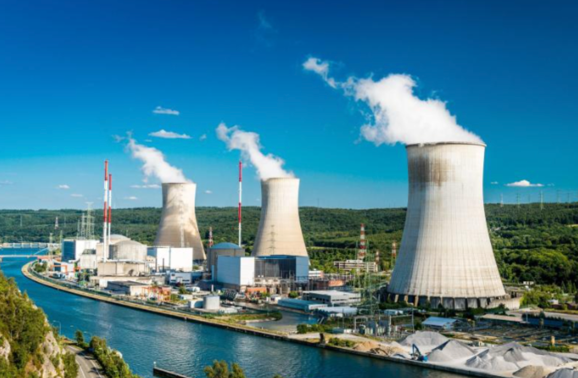 Nuclear power plant with cooling towers releasing steam, next to a river under a blue sky.