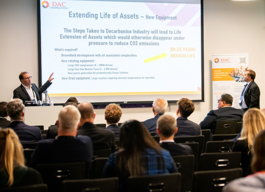 Men presenting at a conference; audience seated, slide titled “Extending Life of Assets”.