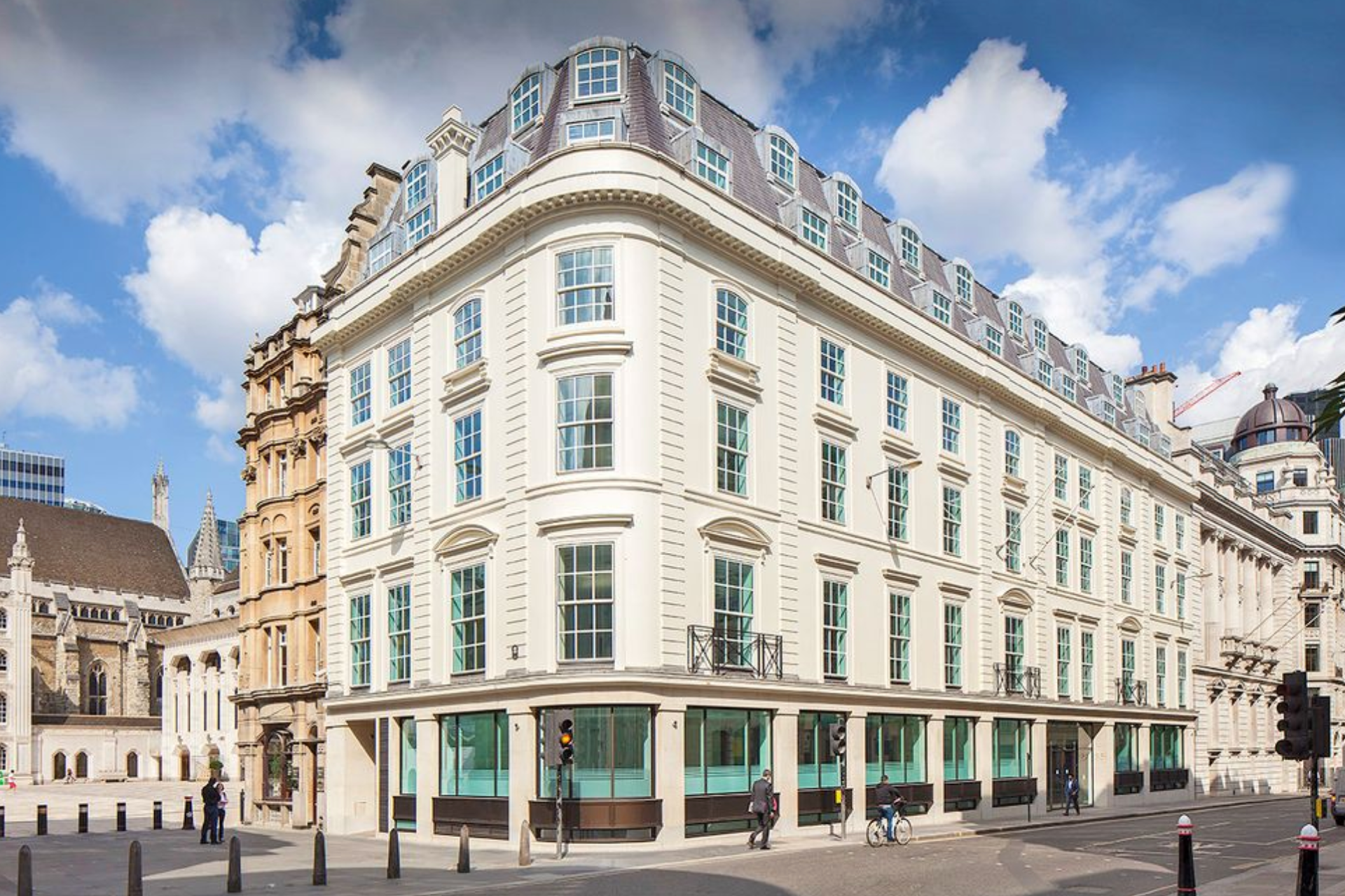 Elegant, cream-colored building with many windows on a city street under a partly cloudy sky.