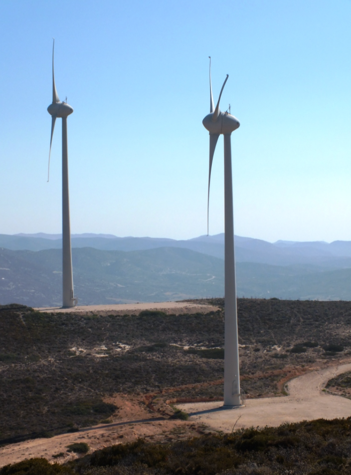 Two wind turbines on a hilltop against a blue sky, one with damaged blades.
