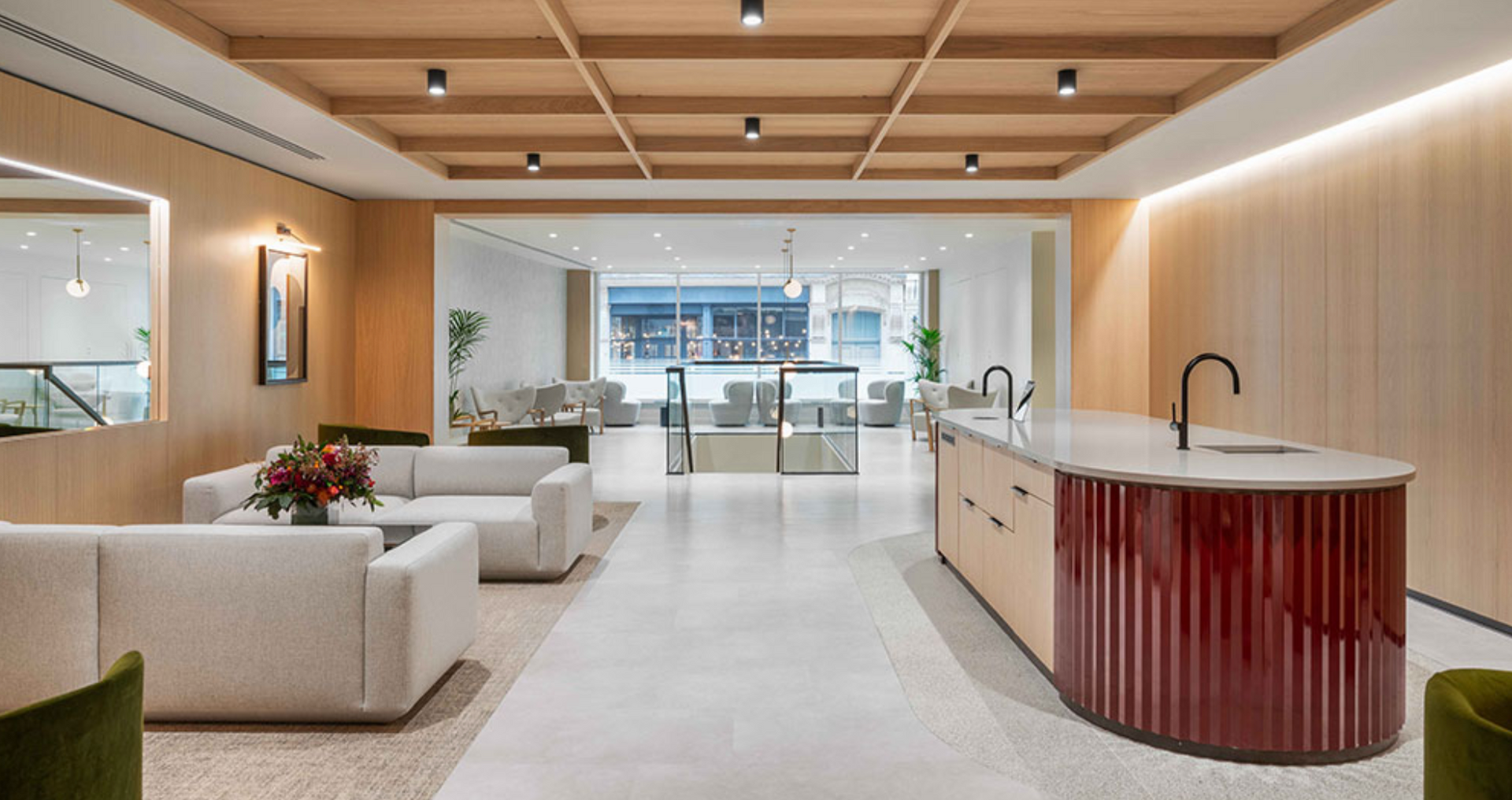 Modern office lounge with white couches, wood paneling, and a red and beige kitchen island.