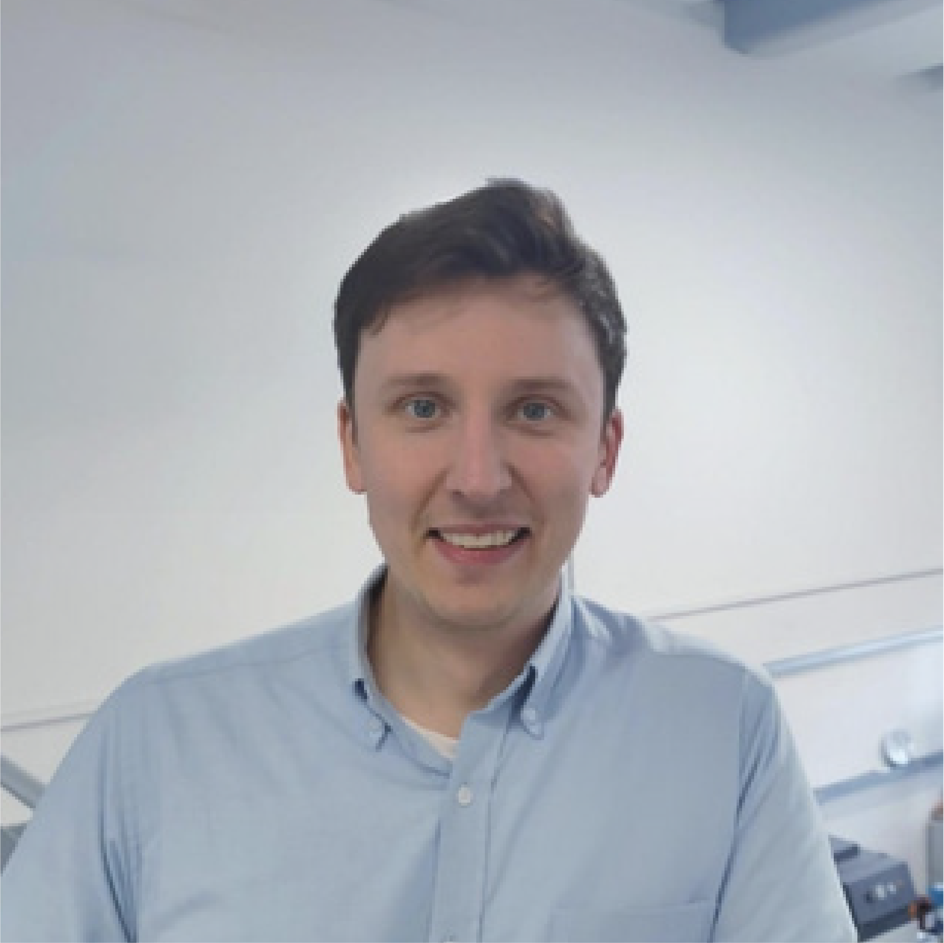 Man in a light blue button-down shirt smiles, indoors.