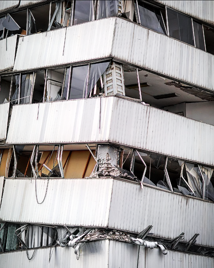 Damaged multi-story building with broken windows and structural damage, angled view.