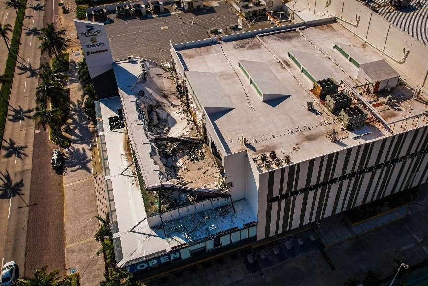 Damaged building roof, collapsed section. Exterior shot of a large commercial structure in daylight.