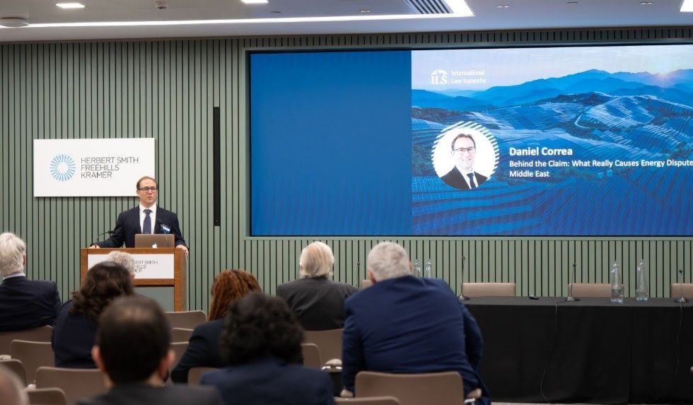 Man speaking at a podium. Presentation screen shows speaker Daniel Carreno's name, title and a mountain scene. Audience seated.