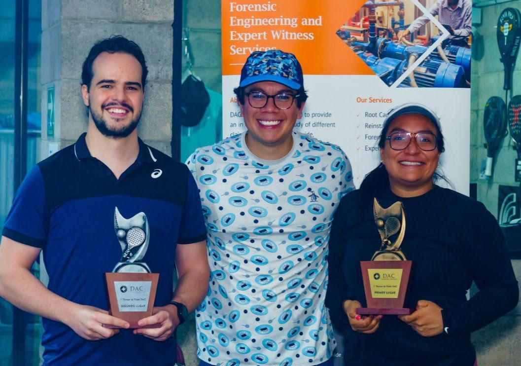 Three people holding trophies, smiling, standing in front of a banner.