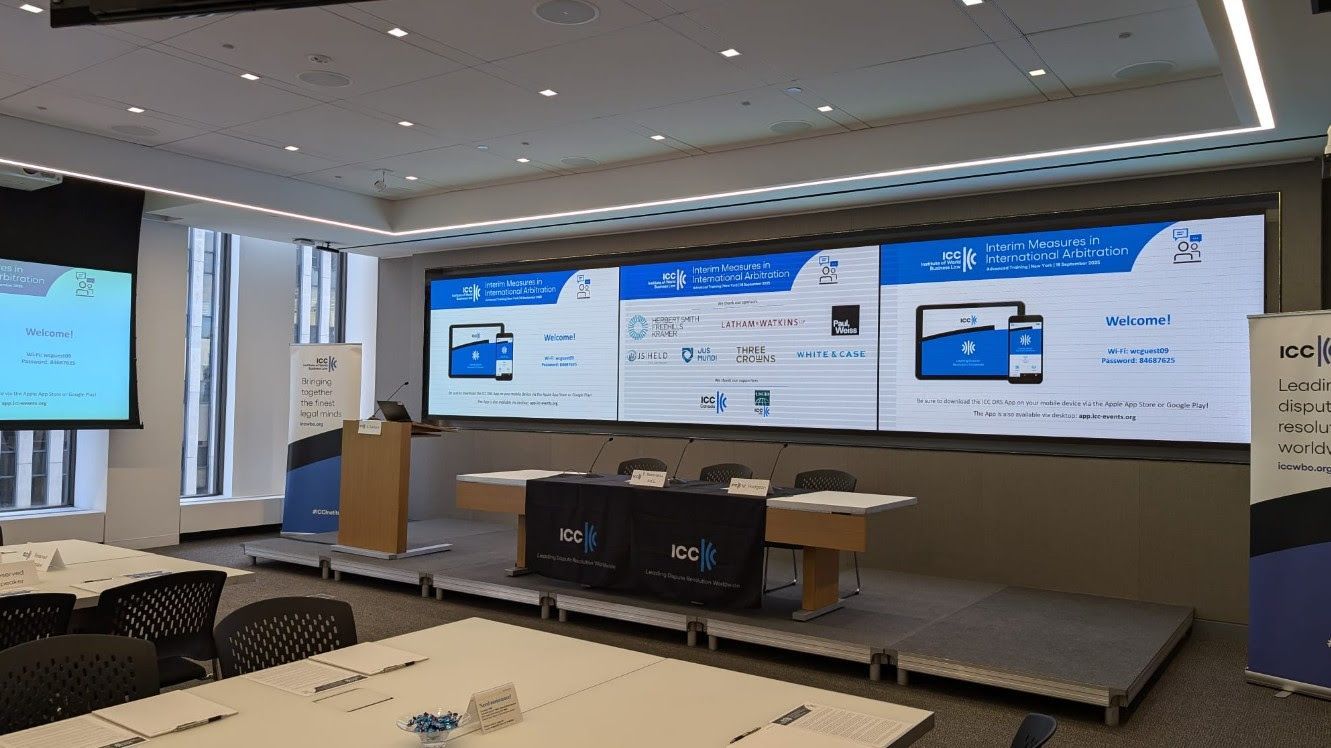 Conference room with a stage, large screen displaying graphics, and tables.