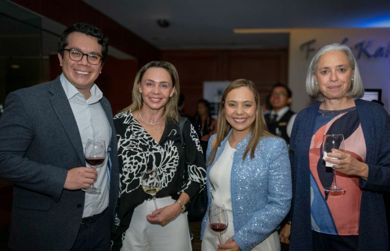 Four people smiling, holding glasses, at an event. A man in a suit, two women in blouses, and another in a blue jacket.
