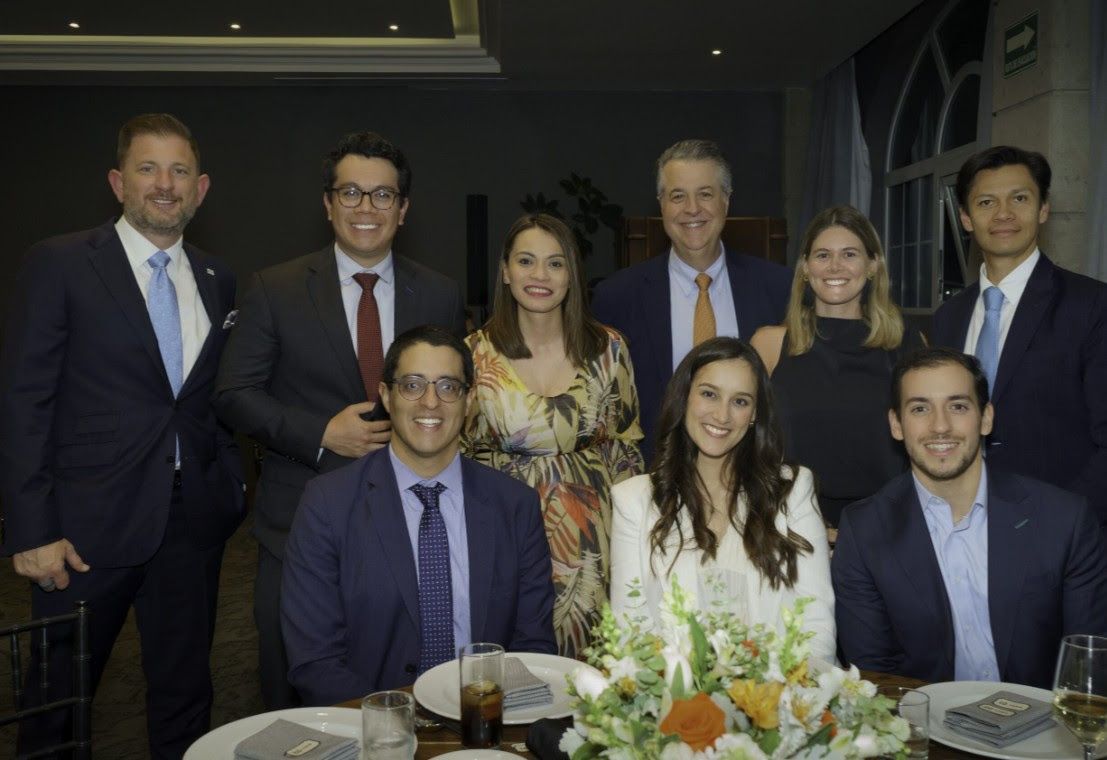 Group of nine people posing for a photo at a formal event, smiling, with a table set in front.