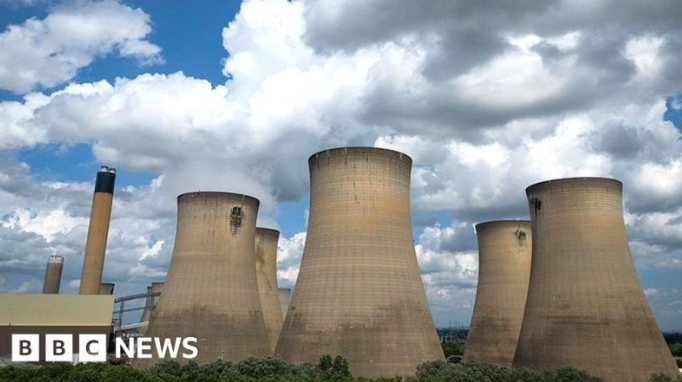 Cooling towers of a power plant with steam billowing under a cloudy sky.