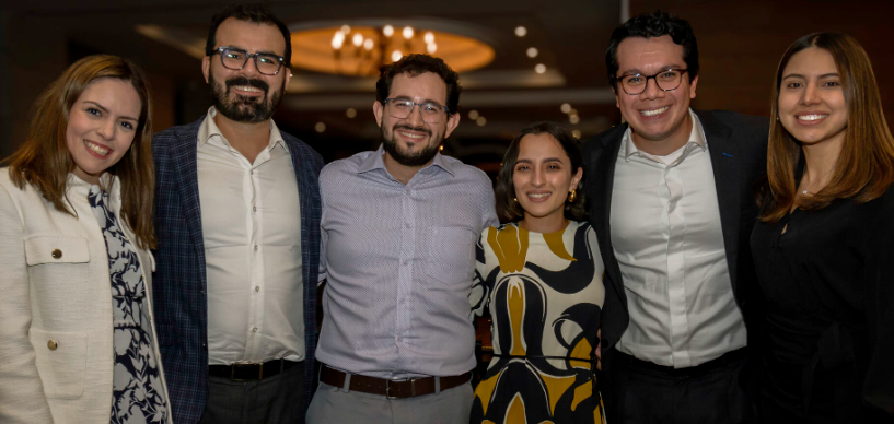 Group of people smiling, posing for a photo. Dim lighting, formal setting.