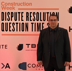 Man in a suit stands in front of a backdrop for a 