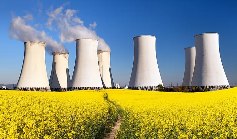 Nuclear power plant with cooling towers in a field of yellow flowers under a clear blue sky.
