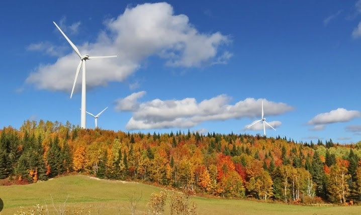 Wind turbines on a colorful autumn hillside under a partly cloudy blue sky.
