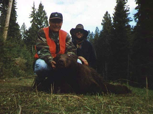 a man in an orange vest is kneeling next to a bear
